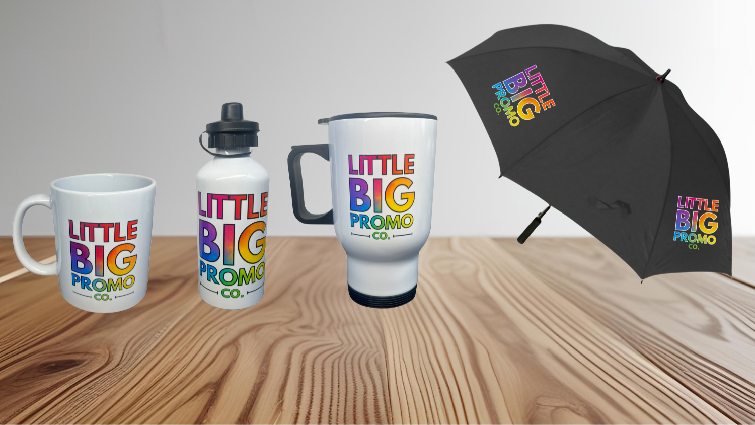 Promotional items including mugs, a water bottle, and an umbrella with 'Little Big Promo Co.' branding on a wooden surface.